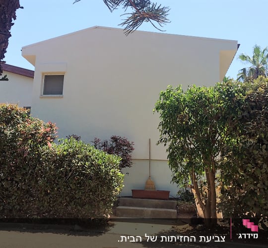 מטאטא ליד קיר בית לבן עם שיחים מסביב
